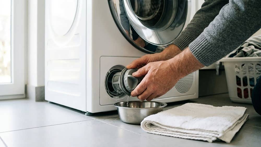 آموزش باز کردن و تمیز کردن فیلتر تخلیه ماشین لباسشویی با قرار دادن حوله و کاسه برای جلوگیری از خیس شدن زمین