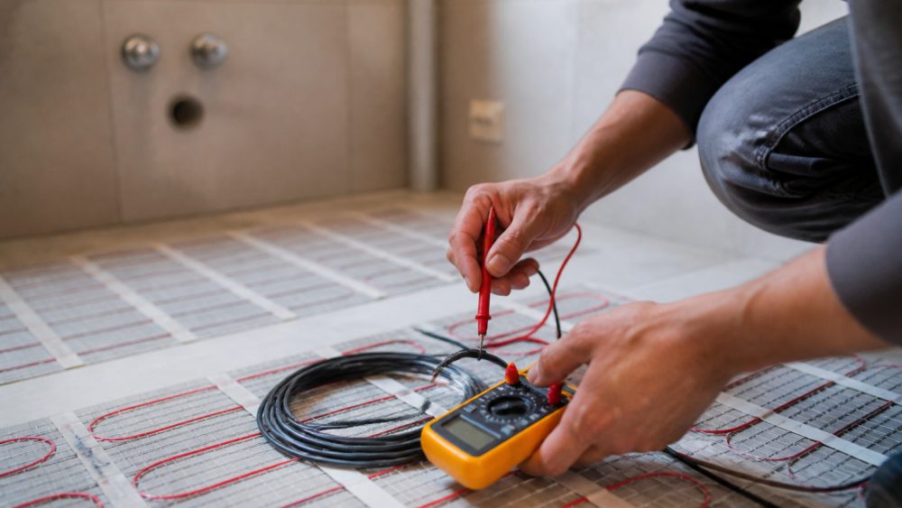 دست تکنسین در حال اندازه گیری مقاومت کابل های گرمایش از کف با مولتی متر روی کف حمام
