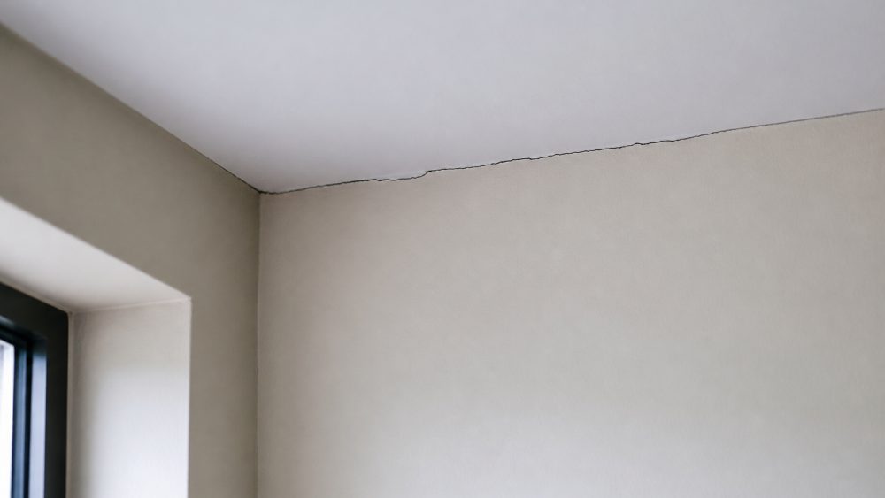 ترک مویی باریک در محل اتصال دیوار گچی سفید و سقف در گوشه یک اتاق روشن