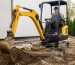 مینی بیل مکانیکی زرد در حال گودبرداری در محوطه یک پروژه ساختمانی کوچک